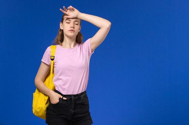 青い壁に黄色のバックパックとピンクのTシャツの女子学生の正面図