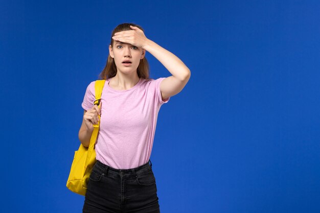青い壁に黄色のバックパックの混乱した表情とピンクのTシャツの女子学生の正面図