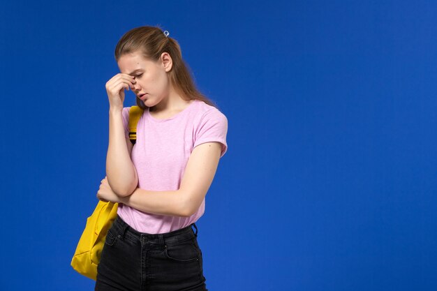 노란색 배낭과 분홍색 티셔츠에 여성 학생의 전면보기 파란색 벽에 우울 소녀