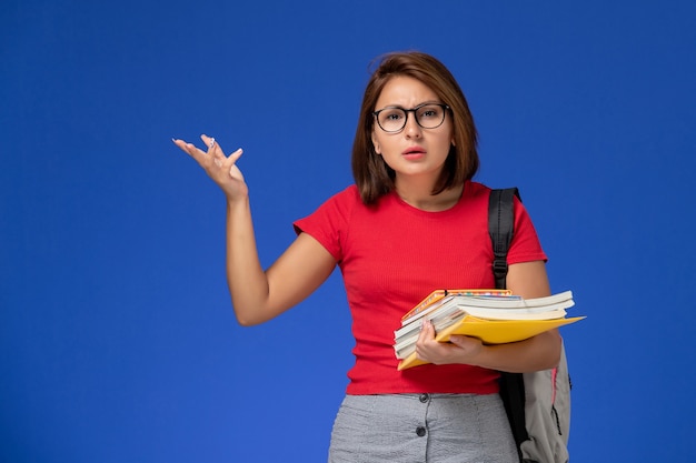 Front view of female student in red shirt with backpack holding books and files