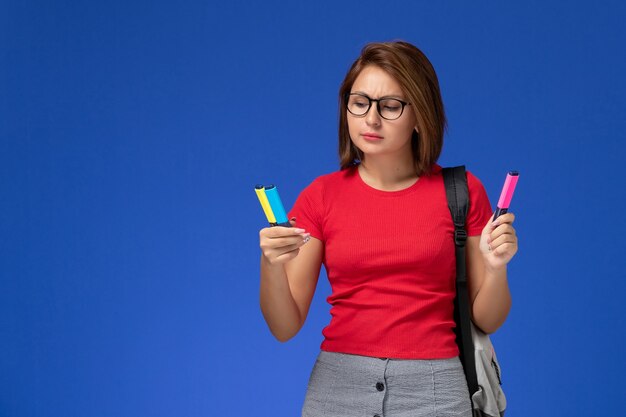 파란색 벽에 펠트 펜을 들고 배낭과 빨간 셔츠에 여성 학생의 전면보기