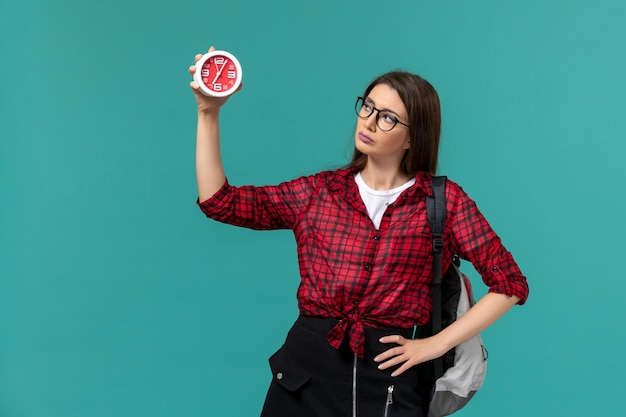 Free photo front view of female student wearing backpack holding clocks on the blue wall