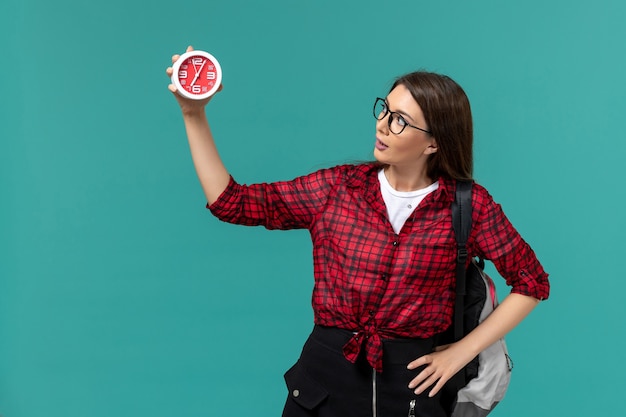 Front view of female student wearing backpack holding clocks on the blue wall