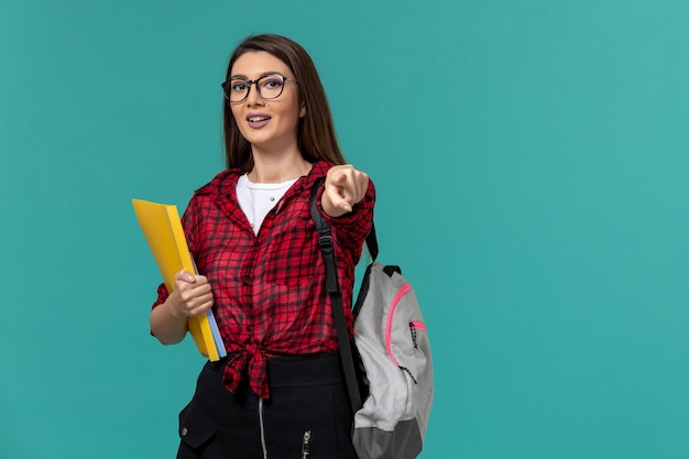 Front view of female student wearing backpack and holding files on blue wall