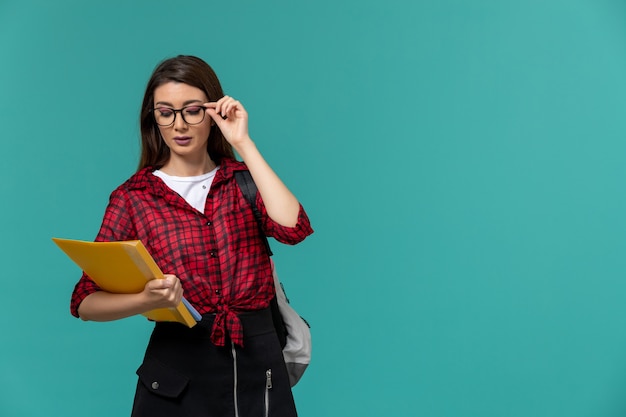 Free photo front view of female student wearing backpack and holding files on light-blue wall