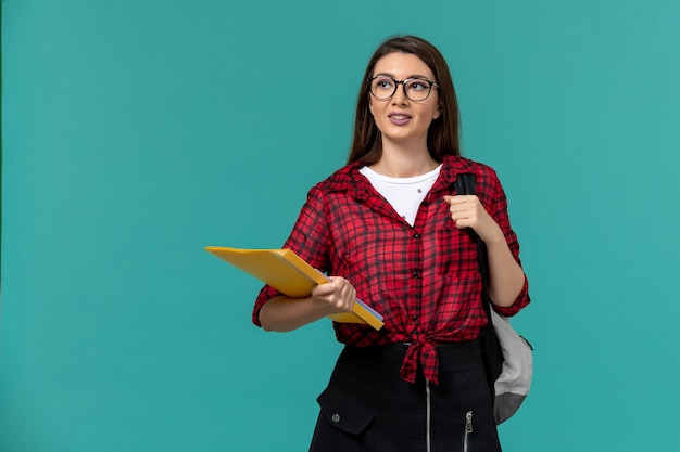 Vista frontale della studentessa che indossa uno zaino e che tiene i file sulla parete azzurra