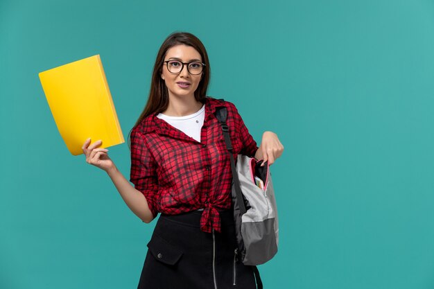 バックパックを身に着けていると水色の壁にファイルを保持している女子学生の正面図