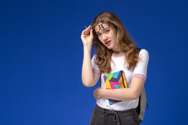 Front view of female student in white shirt holding pen and copybook on blue wall