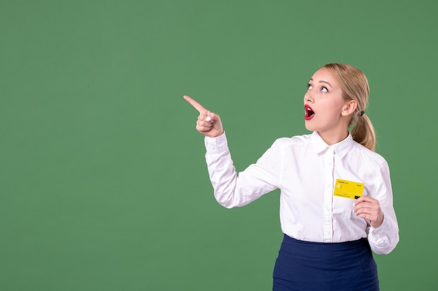 Front view female teacher holding yellow bank card and pointing aside on green