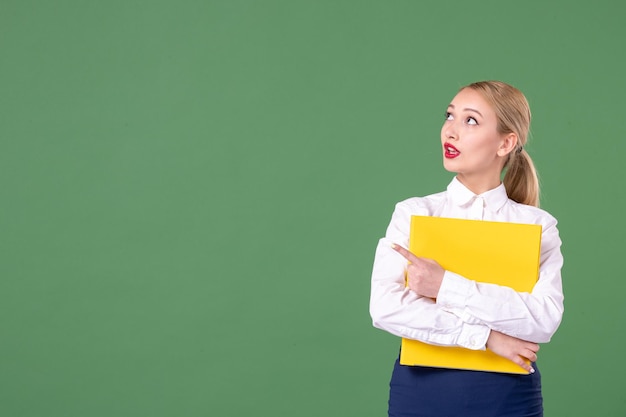 Front view female teacher holding yellow files on green background book study uniform lesson student school work university woman