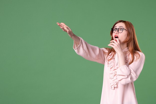 Insegnante femminile di vista frontale in camicetta rosa che punta con la faccia spaventata su sfondo verde lavoro scuola donna giovane studente biblioteca lavoro libro lezione colore college