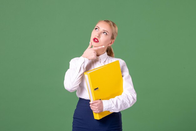 Front view female teacher posing in strict clothes with yellow files on green background work student book school woman library lesson study