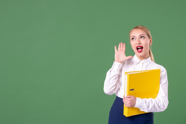 Front view female teacher posing with yellow files on green background book school library study university uniform work student woman lesson