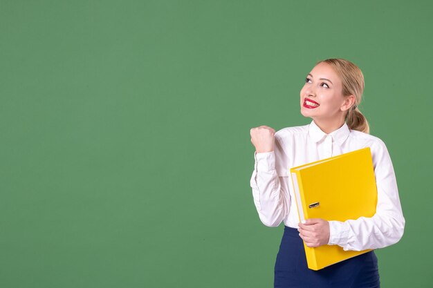 Front view female teacher posing with yellow files on green background book school woman library study university uniform work lesson