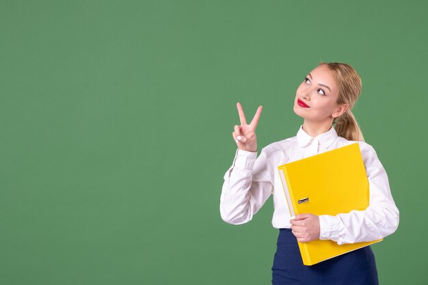Front view female teacher posing with yellow files on green background school library study lesson university uniform woman book work students