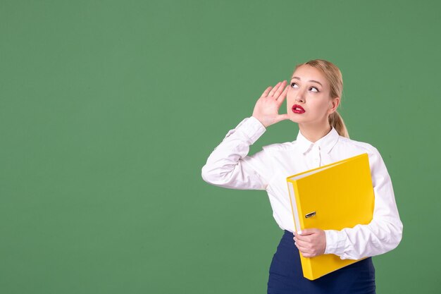 Front view female teacher posing with yellow files on green background school library study university uniform work student woman lesson