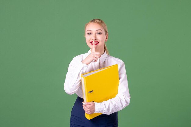 Front view female teacher in strict clothes with yellow files on green background student university woman book study library school work lessons