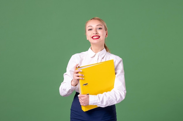 Вид спереди учительница в строгой одежде с желтыми файлами на зеленом
