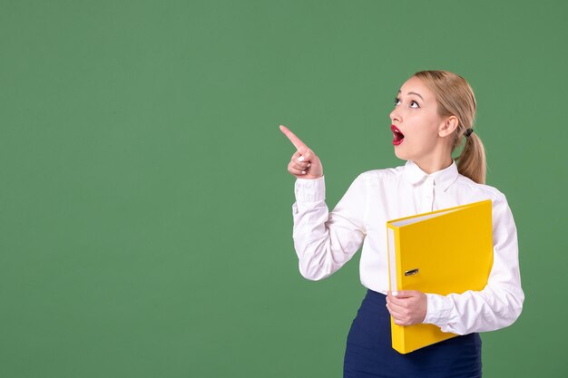 Front view female teacher with yellow files on green background lesson work student university book study library uniform school