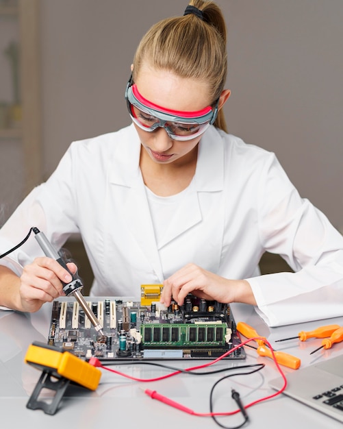 Front view of female technician with soldering iron and electronics board