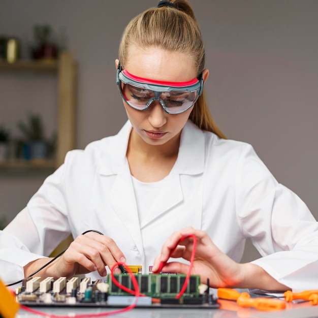 Front view of female technician with soldering iron and electronics motherboard