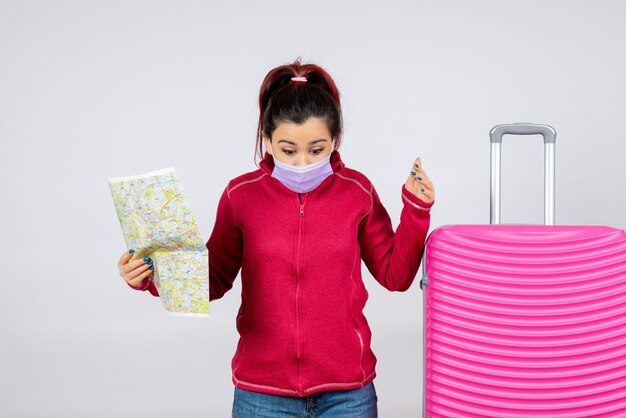 Front view female tourist holding map in mask on a white wall