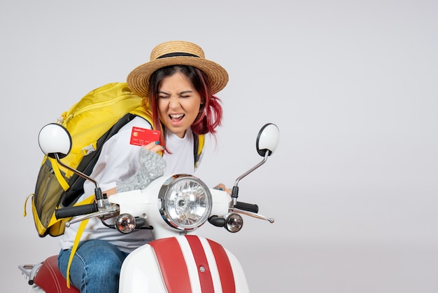 Front view female tourist sitting on motorcycle holding bank card white wall 