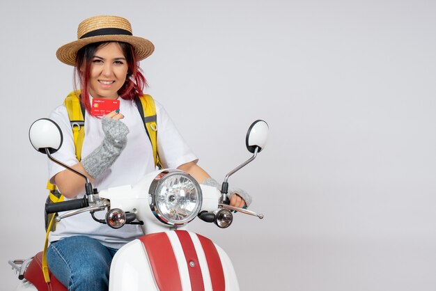 Front view female tourist sitting on motorcycle holding bank card white wall