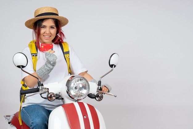 Front view female tourist sitting on motorcycle holding bank card white wall