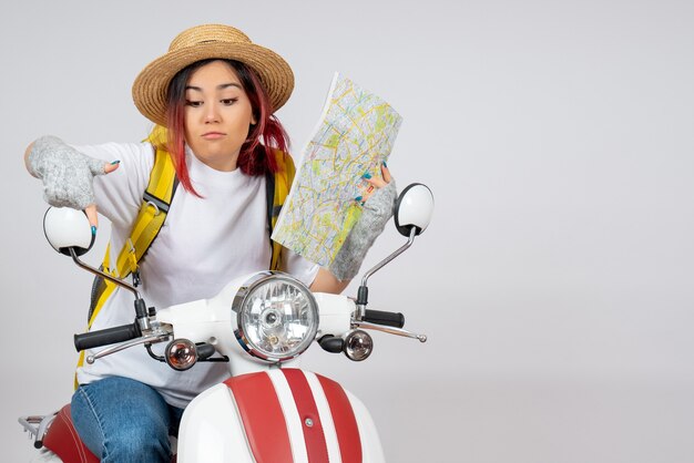 Front view female tourist sitting on motorcycle holding map white wall