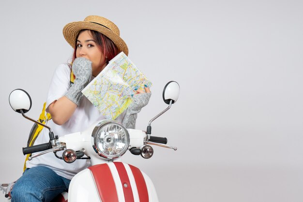 Вид спереди туристка сидит на мотоцикле, держа карту белой стене