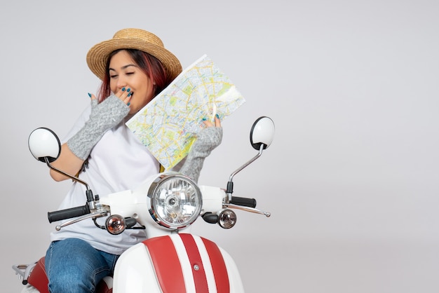 Front view female tourist sitting on motorcycle holding map white wall