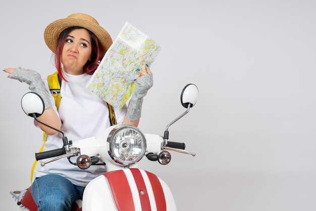 Front view female tourist sitting on motorcycle holding map white wall