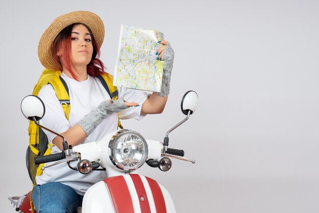 Front view female tourist sitting on motorcycle holding map white wall