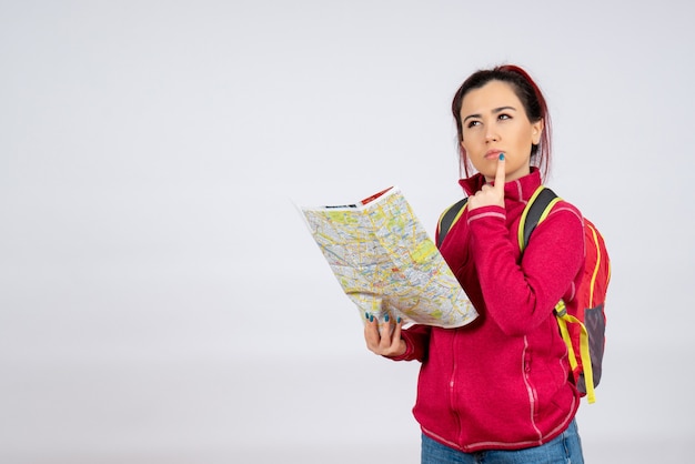 Front view female tourist with backpack and map on white wall