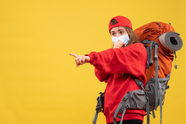 Front view female tourist with backpack and mask pointing with finger something