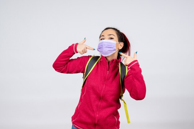 Front view female tourist with backpack in mask on white wall