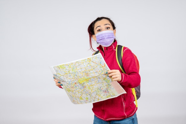 Front view female tourist with map in mask on a white wall