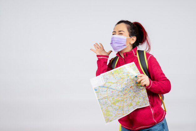 Front view female tourist with map in mask on white wall