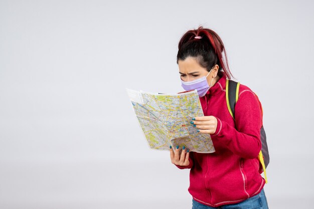 Front view female tourist with map in mask on white wall