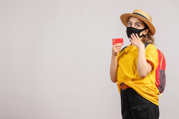 Front view of female traveller with backpack holding up card on grey wall