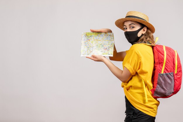 Front view of female traveller in yellow t-shirt holding map on white wall