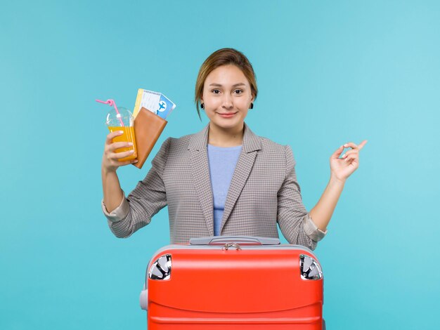 青い背景の海の旅の休暇の飛行機の航海旅行で飲み物とチケットを保持している休暇中の女性の正面図