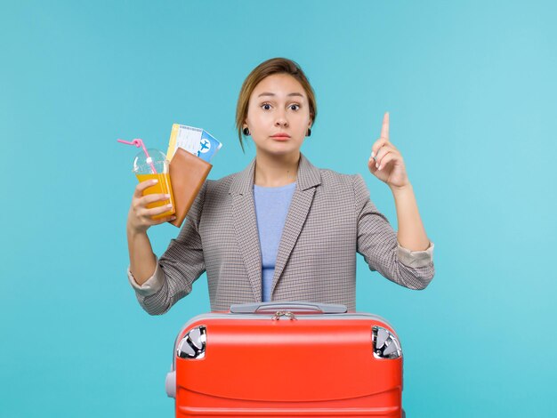 青い背景の海の旅の休暇の航海旅行で飲み物とチケットを保持している休暇中の女性の正面図