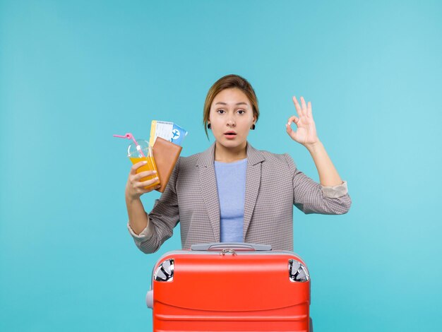 青い背景の海の旅の休暇の航海旅行で新鮮な飲み物とチケットを保持している休暇中の女性の正面図