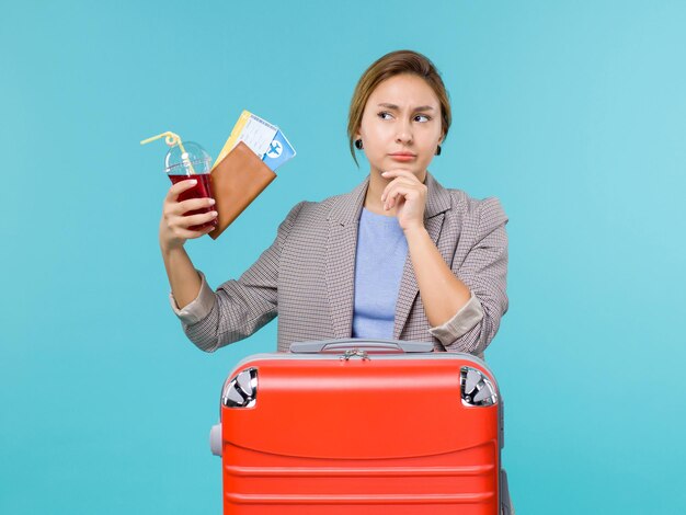 Вид спереди женщина в отпуске, держащая свежий стакан сока и билеты на синем полу, путешествие на самолете, отпуск, путешествие, путешествие на море