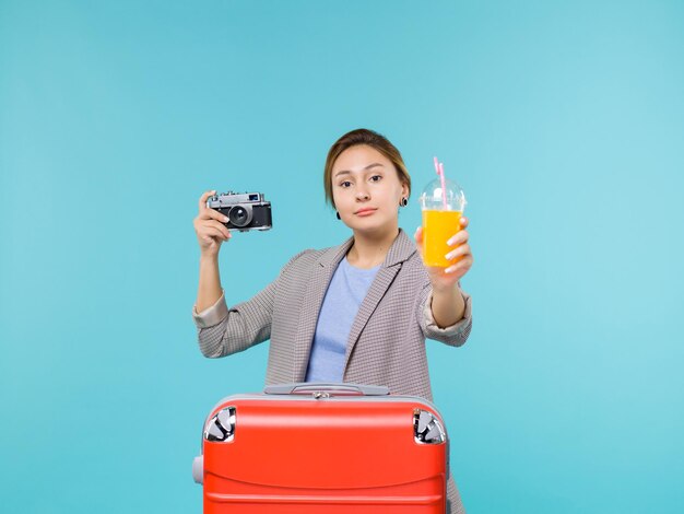 Front view female in vacation holding fresh juice and camera on the light blue background sea vacation voyage journey trip