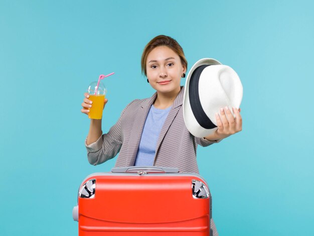 Front view female in vacation holding fresh juice and her hat on light blue background voyage sea vacation journey trip