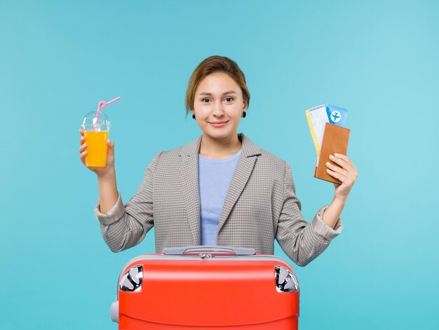 青い背景の海の休暇の飛行機の航海旅行の旅でフレッシュジュースとチケットを保持している休暇中の女性の正面図