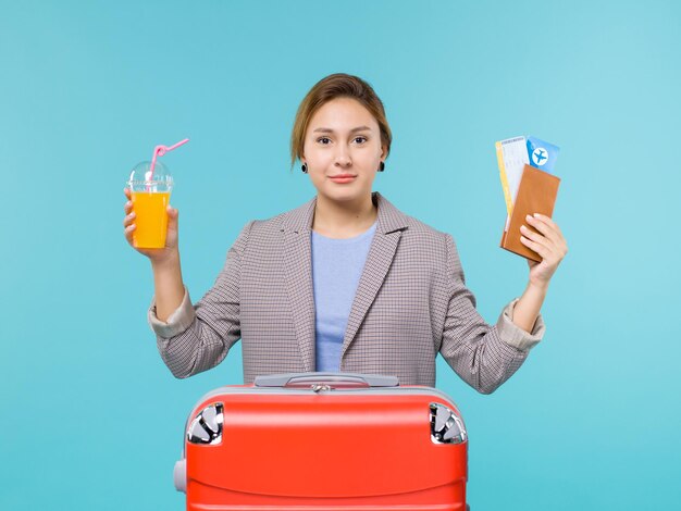 Вид спереди женщина в отпуске, держащая свежий сок и билеты на синем фоне, море, отпуск, самолет, путешествие, путешествие, путешествие